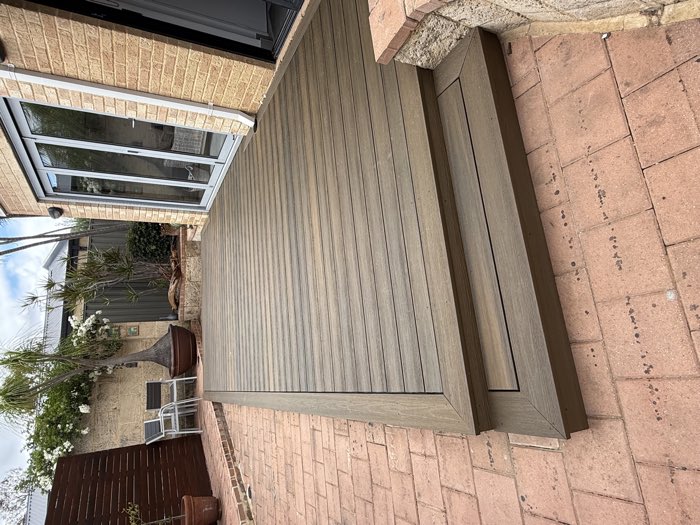 Composite deck with steps down to brick paving beside a brick home